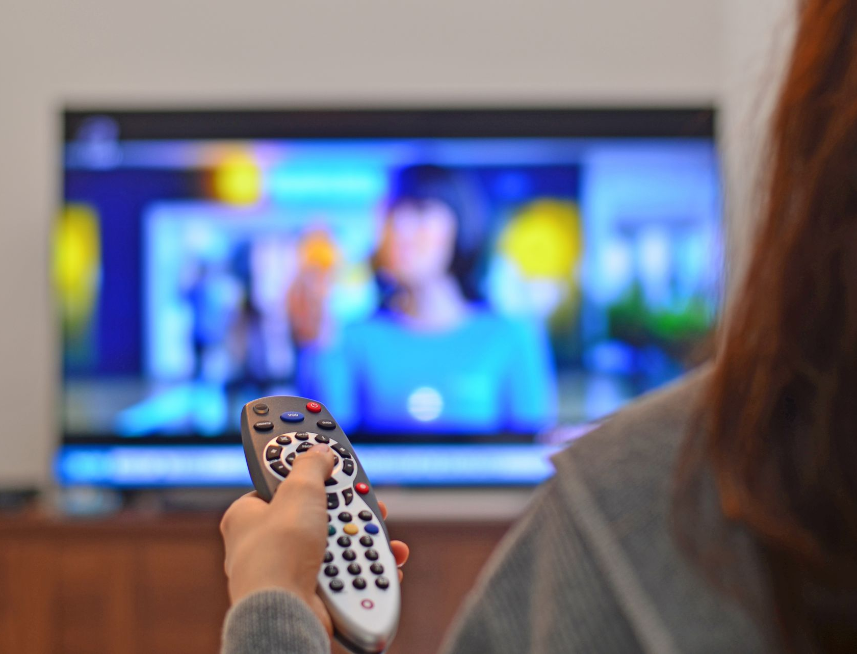 Une personne tenant une télécommande, la pointant vers un écran de télévision.
