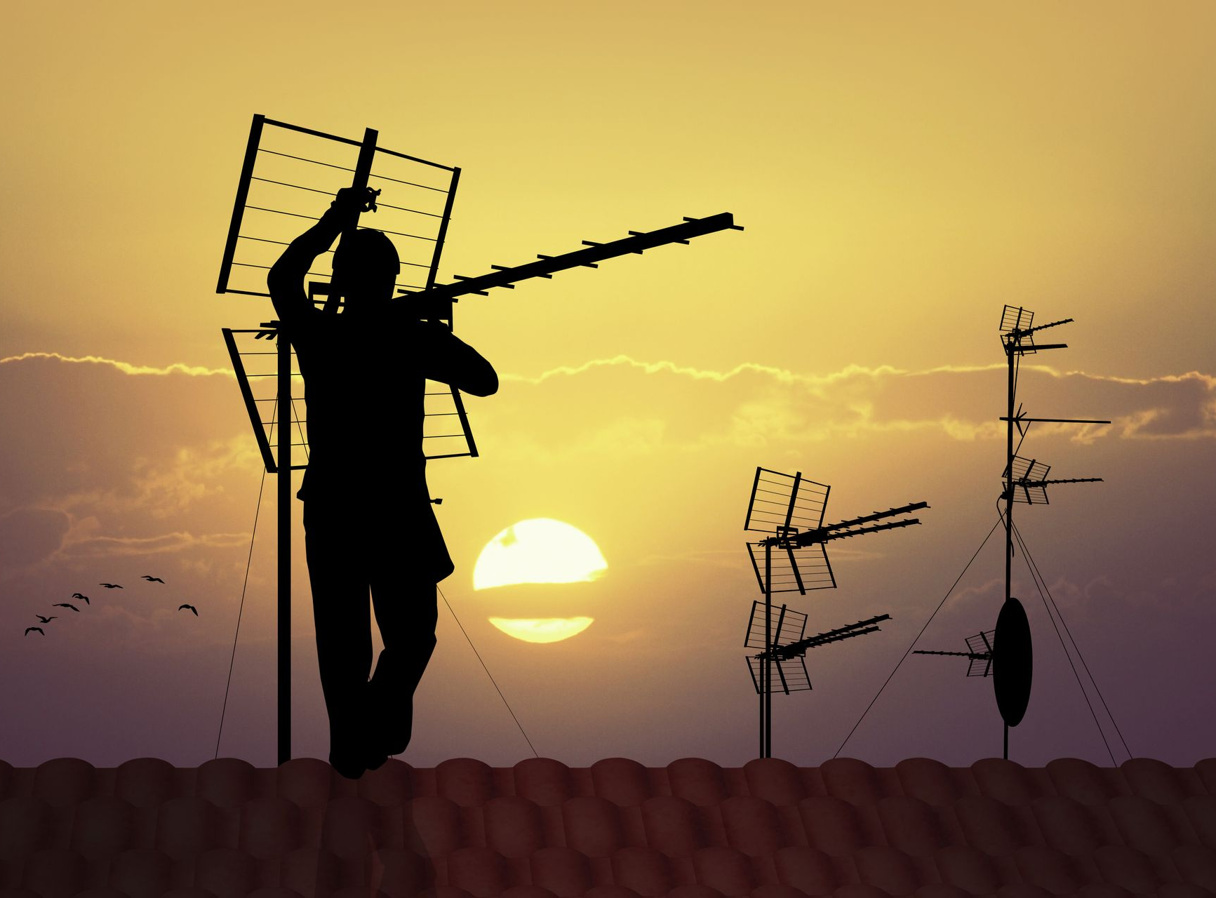 Silhouette d'une personne installant une antenne de télévision sur un toit au coucher du soleil.