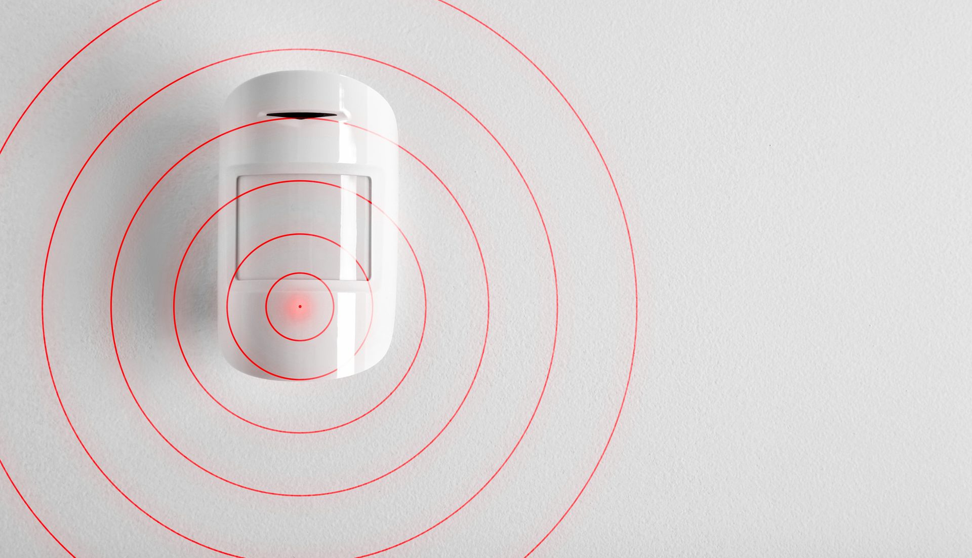 Détecteur de mouvement blanc fixé au mur, émettant des cercles de détection rouges.