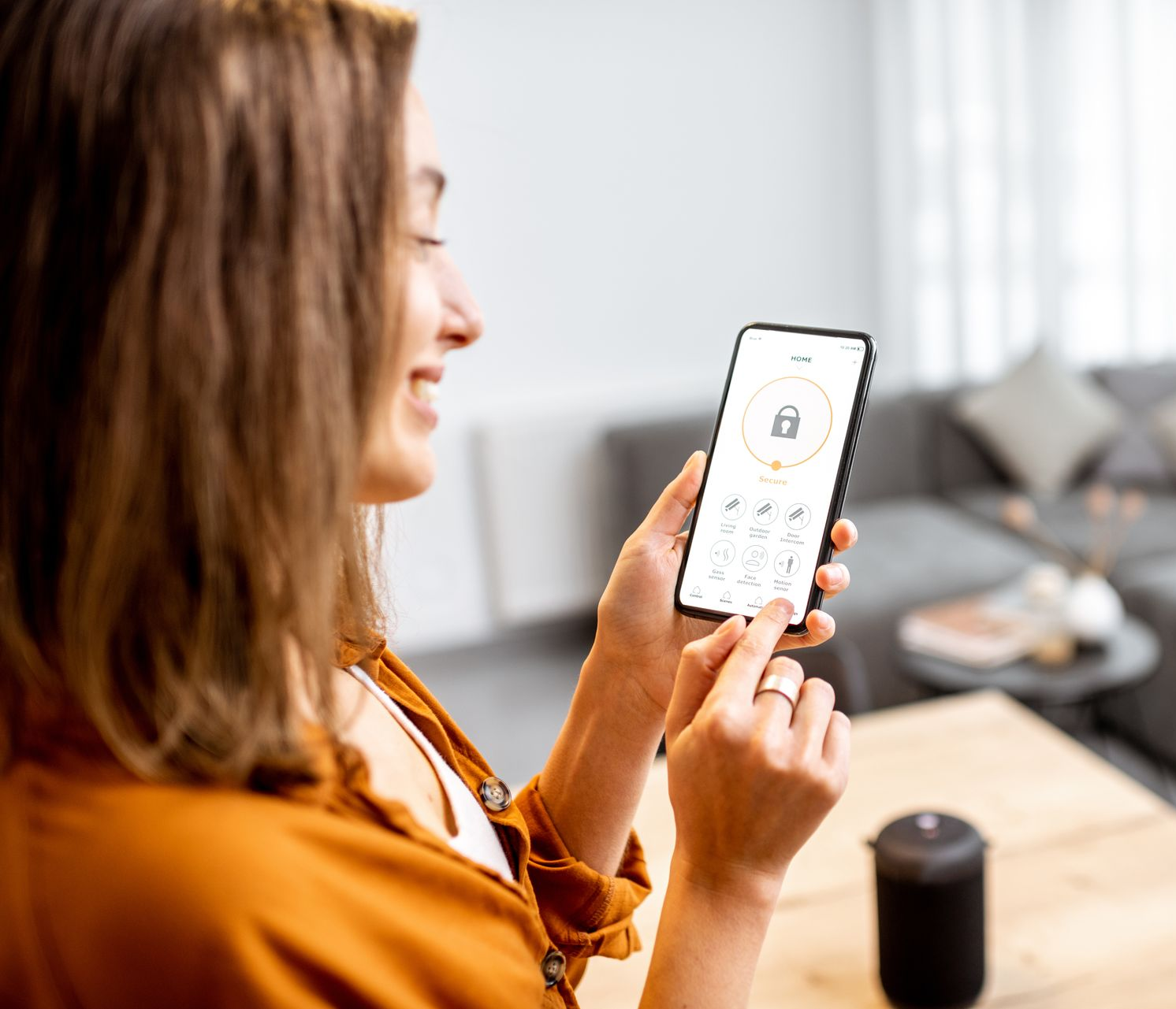 Femme souriante, utilisant un smartphone pour gérer un appareil domotique.