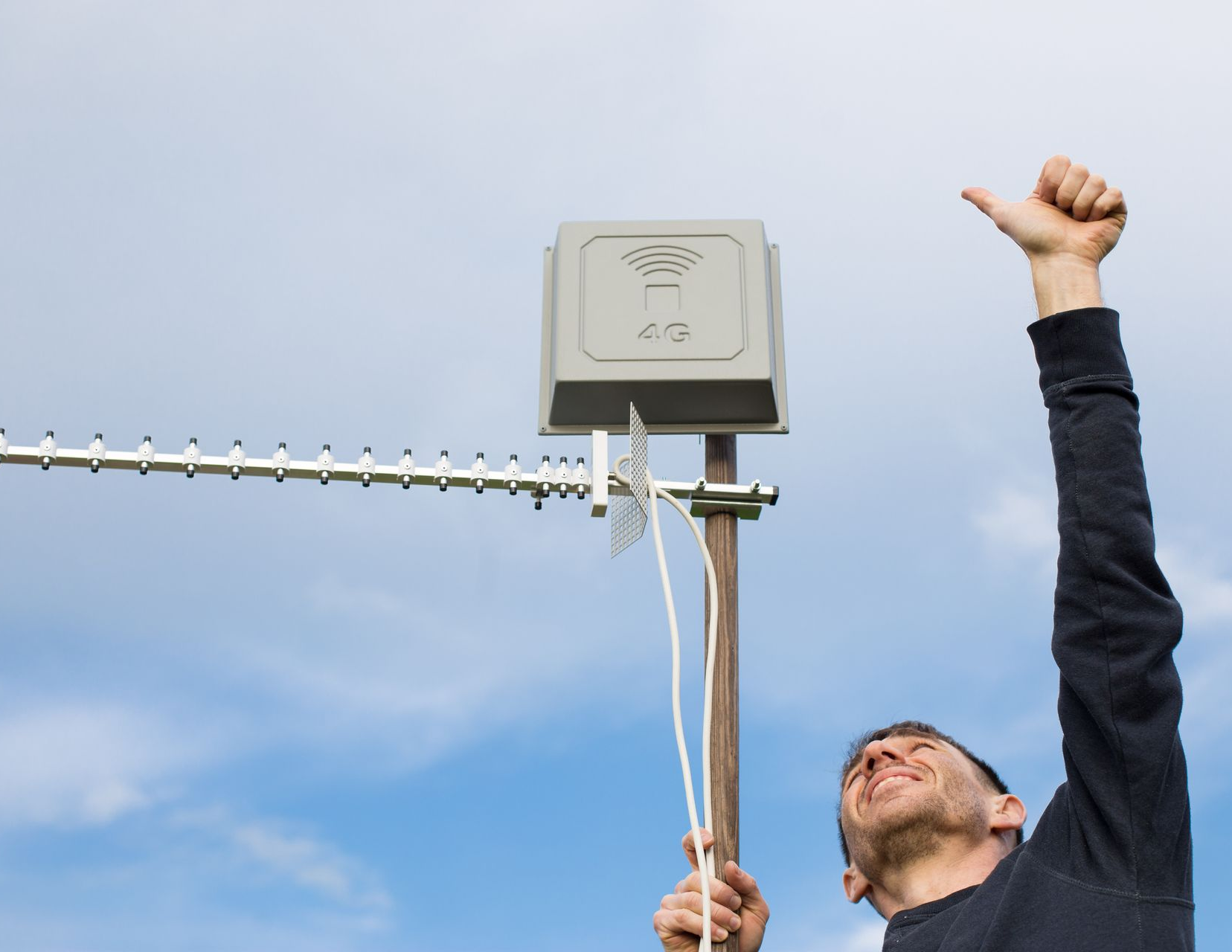 Un homme fait un signe de pouce levé à côté d'une antenne et d'un amplificateur de signal 4G.