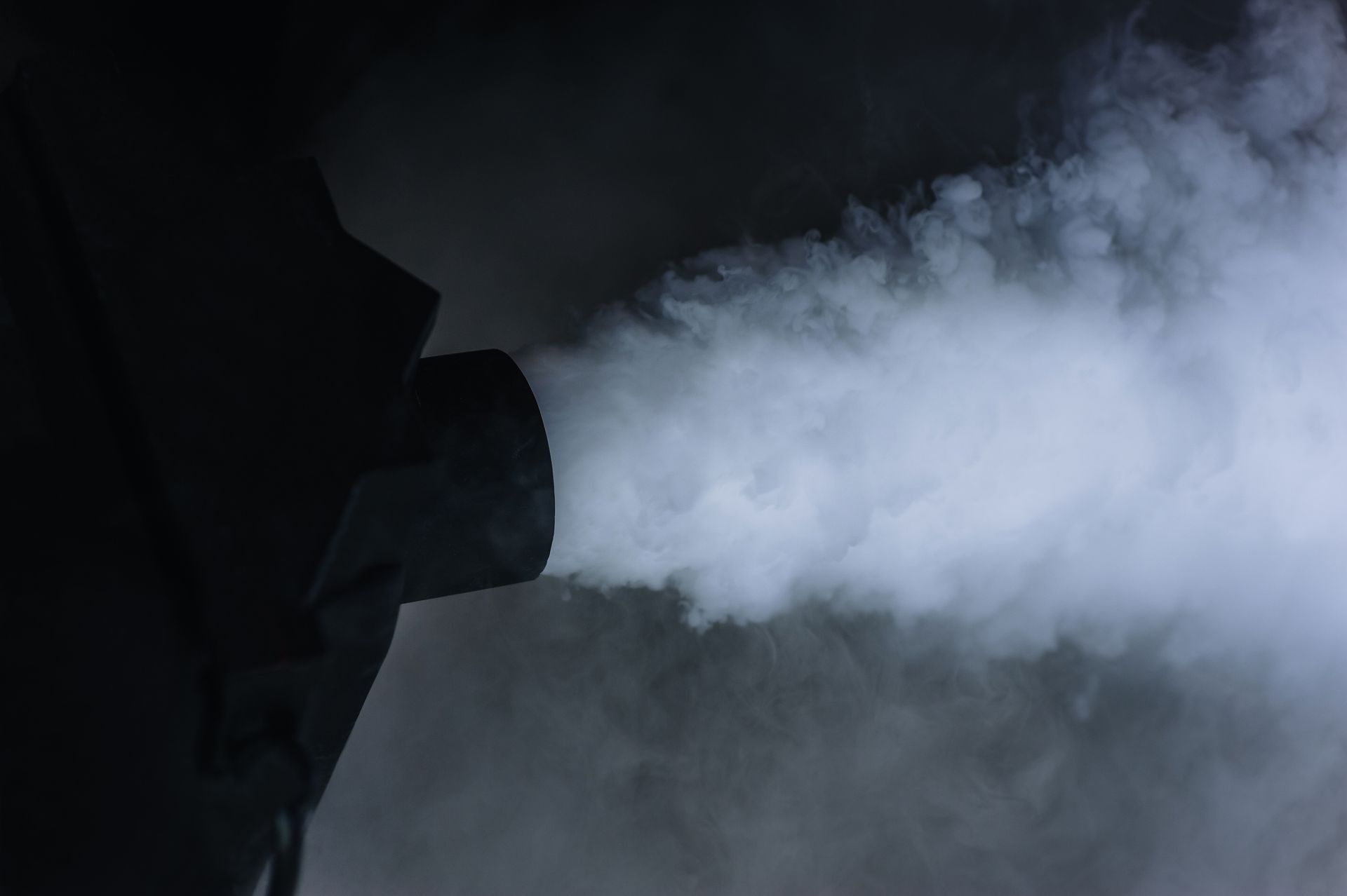 Objet noir expulsant de la fumée blanche dans un environnement sombre.