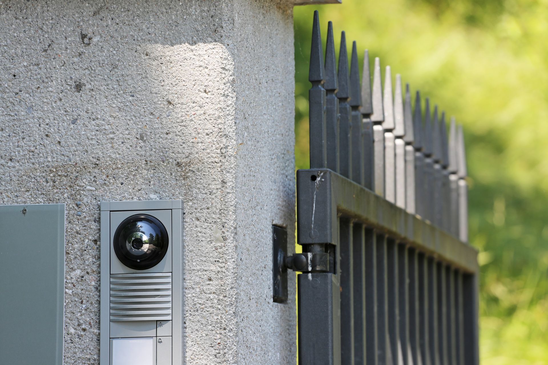 Caméra de sécurité et interphone sur un mur gris, à côté d'un portail métallique noir.