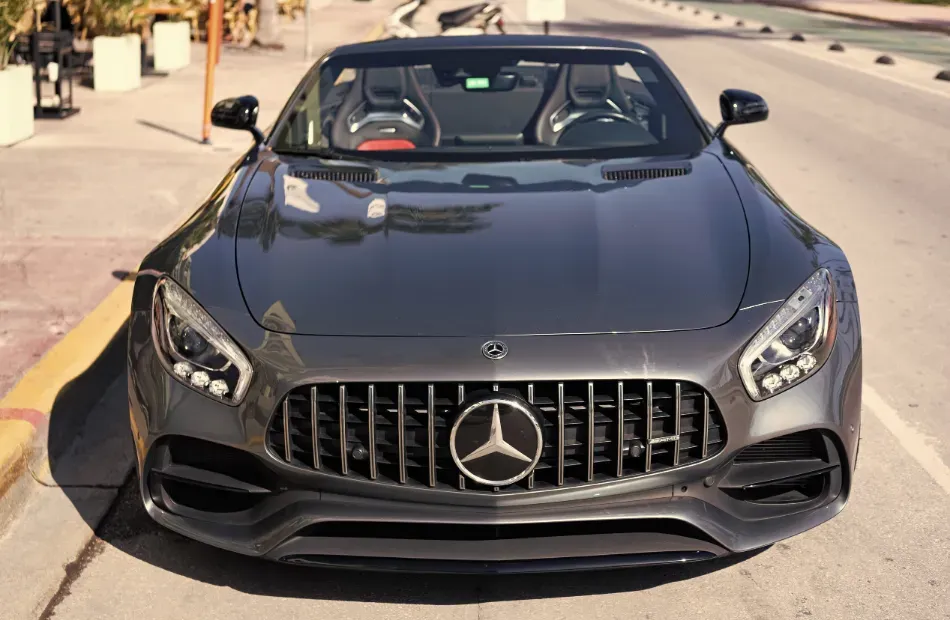 Vista frontal de un Mercedes-Benz deportivo gris oscuro estacionado en una calle soleada.