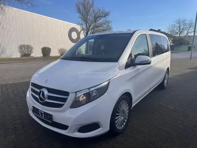 Furgoneta Mercedes blanca aparcada al aire libre cerca de un edificio en un día soleado.