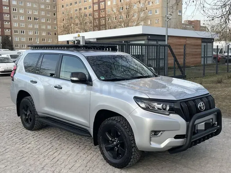 SUV plateado con ruedas negras estacionado en un terreno pavimentado cerca de edificios de apartamentos.