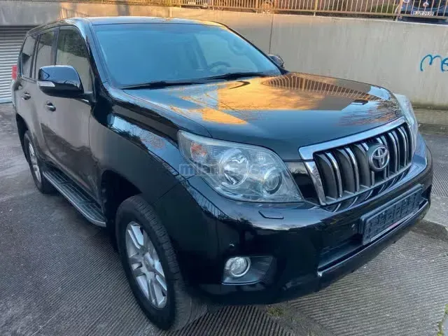 SUV Toyota negro estacionado en una calle junto a un muro de hormigón, vista frontal izquierda.