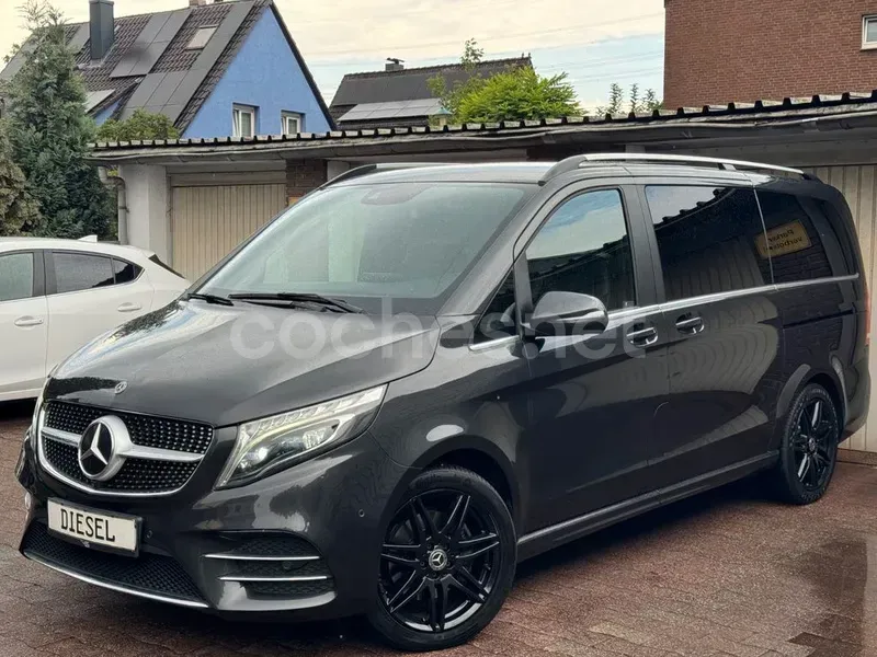 Una furgoneta Mercedes de color gris oscuro aparcada en una entrada de garaje junto a un coche blanco, con casas al fondo.