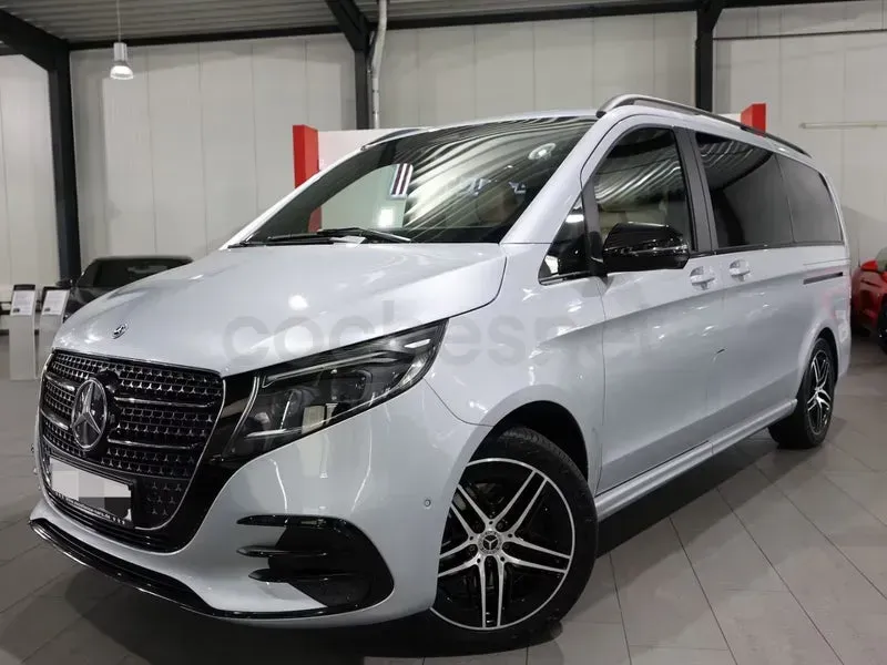 Minivan Mercedes plateada estacionada en el interior, vista frontal izquierda en una sala de exposición o garaje.