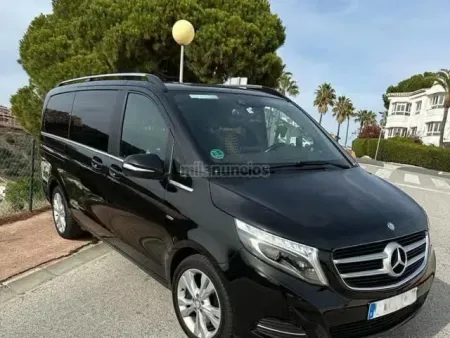 Furgoneta Mercedes negra aparcada en una calle junto a árboles y casas, con cristales tintados y detalles plateados.