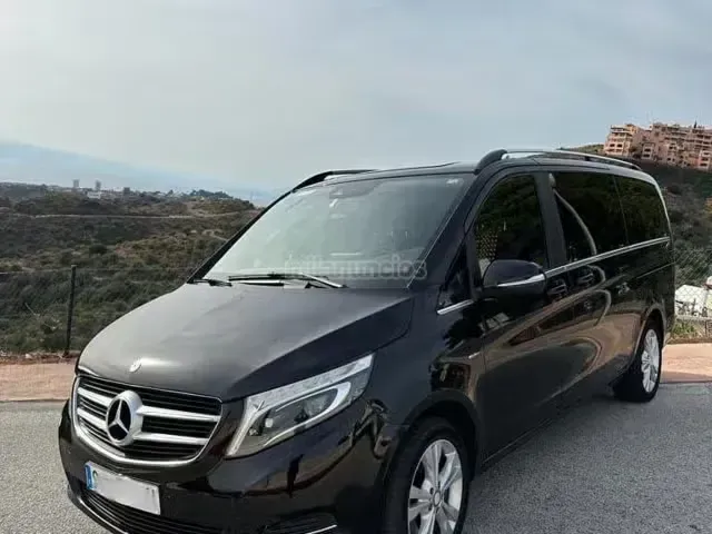 Furgoneta Mercedes negra aparcada al borde de una carretera con vistas a un paisaje montañoso.