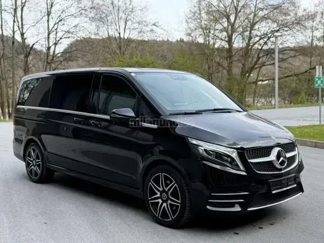 Furgoneta Mercedes negra aparcada en una carretera mojada junto a unos árboles en un día nublado.