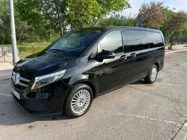 Furgoneta Mercedes negra aparcada al borde de la carretera, con árboles al fondo.
