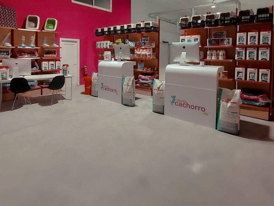 Interior de una tienda de mascotas con mostradores blancos, estantes de comida para mascotas y una pared de color rosa brillante.