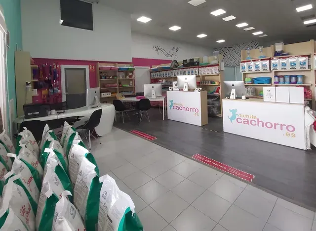 Interior de una tienda de mascotas con mostradores blancos, estantes de productos y bolsas de comida para mascotas en primer plano.