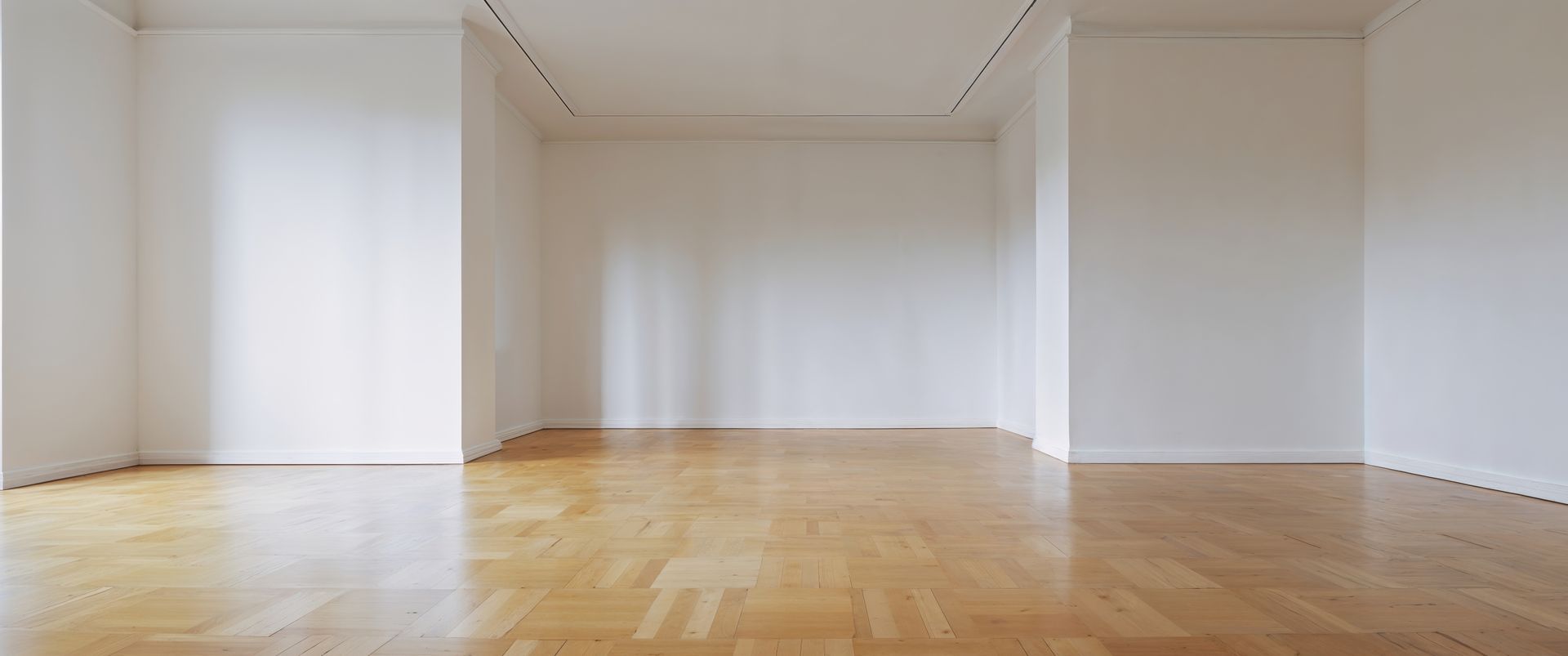Pièce vide avec parquet clair et murs blancs.