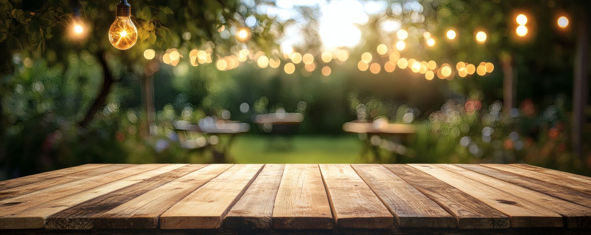 Terrasse en bois au premier plan avec un arrière-plan flou de fête de jardin, des guirlandes lumineuses et des tables.