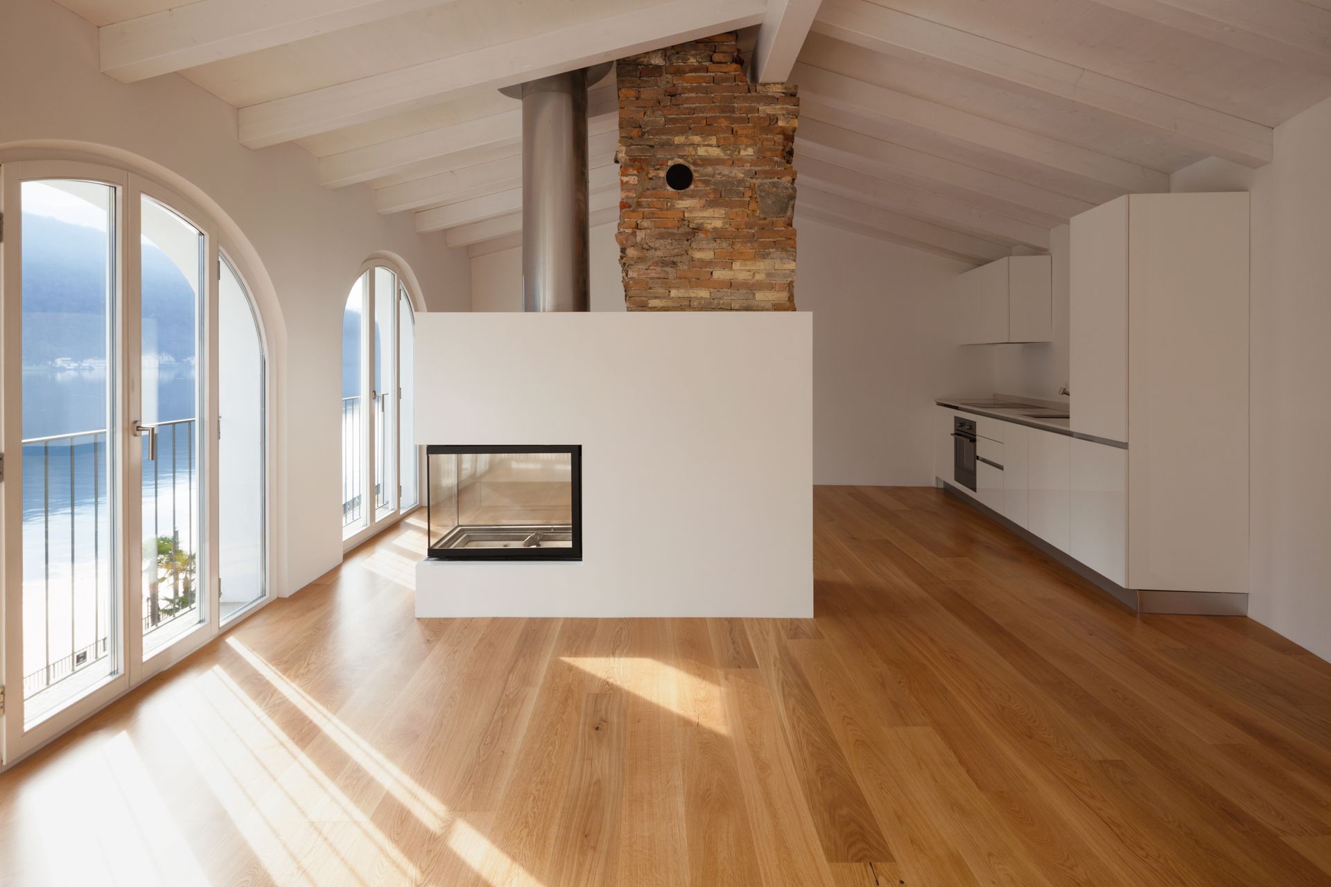 Intérieur spacieux et lumineux avec fenêtres cintrées, cheminée, parquet et cuisine simple.