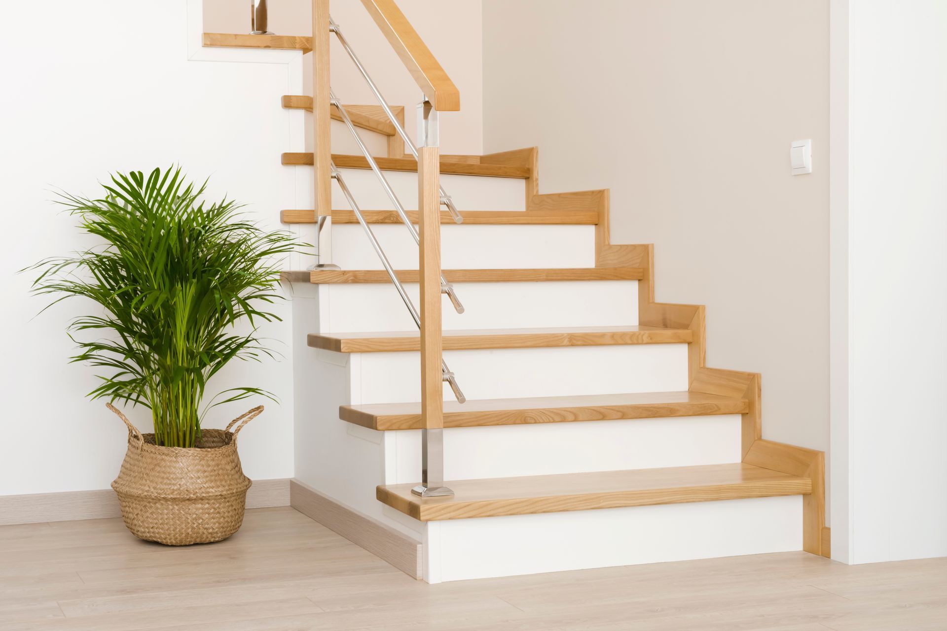 Escalier en bois avec contremarches blanches, rampe en acier inoxydable et plante en pot.