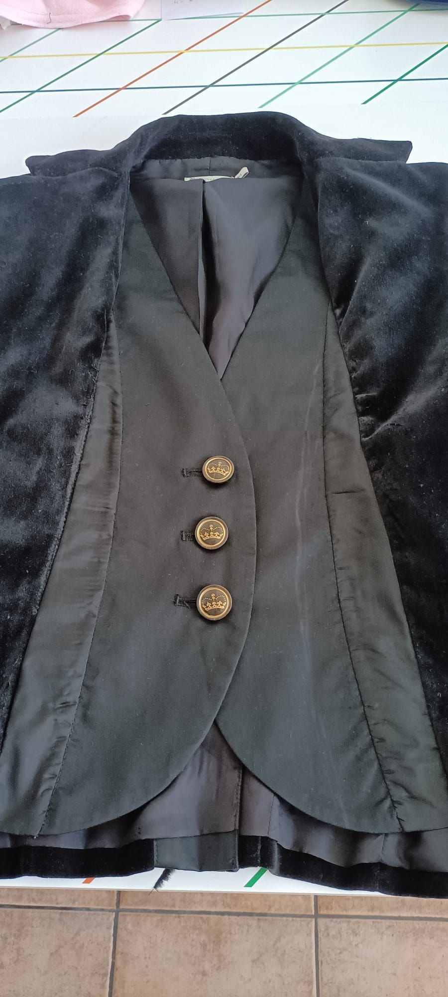 Un blazer negro con aspecto de terciopelo y una inserción gris oscuro estilo chaleco con tres botones dorados, extendido sobre una superficie plana.