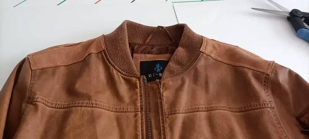 Vista de cerca del cuello y los hombros de una chaqueta bomber de color tostado, confeccionada en piel sintética.