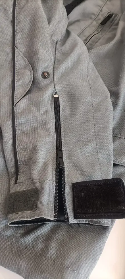 Manga de chaqueta de tela gris texturizada con cremallera negra y cierre de velcro en el puño.