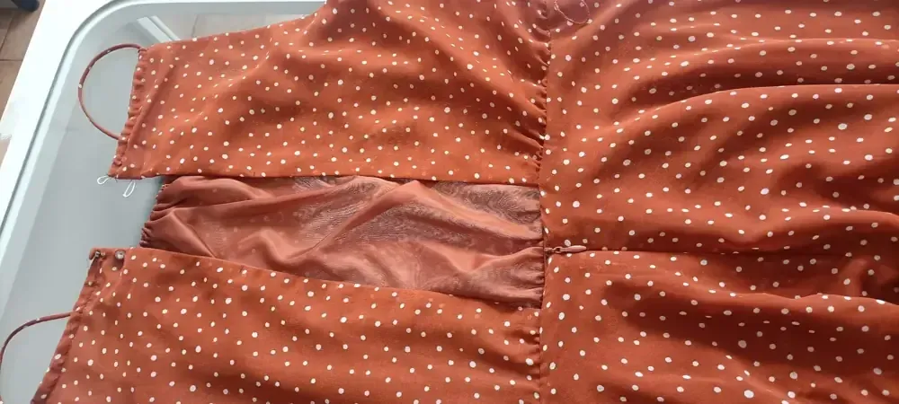 Un vestido color óxido con lunares blancos que presenta una abertura en la cintura con tela a la vista.