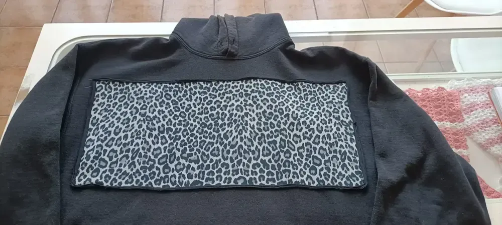 Una sudadera negra con un parche ancho y rectangular con estampado de leopardo gris y negro cosido en el pecho.
