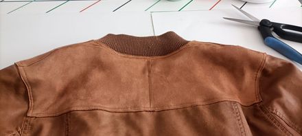 El cuello y la parte trasera de una chaqueta de imitación de ante marrón descansan sobre una superficie blanca, con unas tijeras cerca.