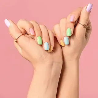Manos de mujer con uñas de colores y anillos sobre un fondo rosa.