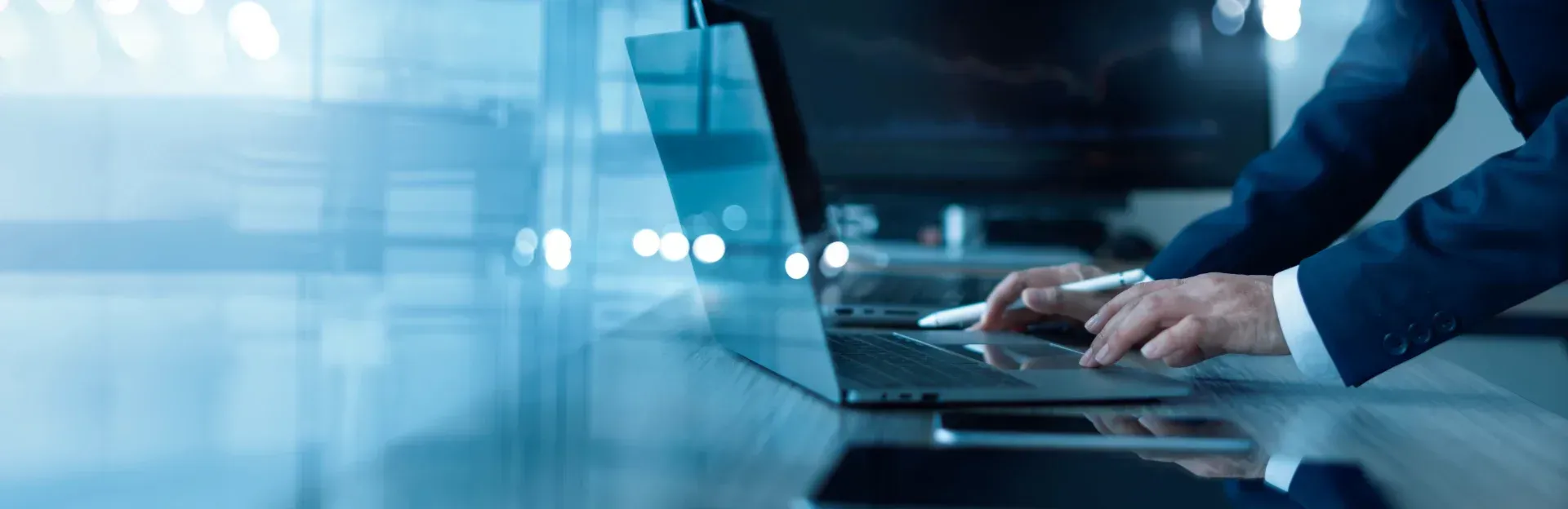 Eine Person tippt in einem modernen Büro auf einem Laptop. Kühle Blautöne und unscharfer Hintergrund.