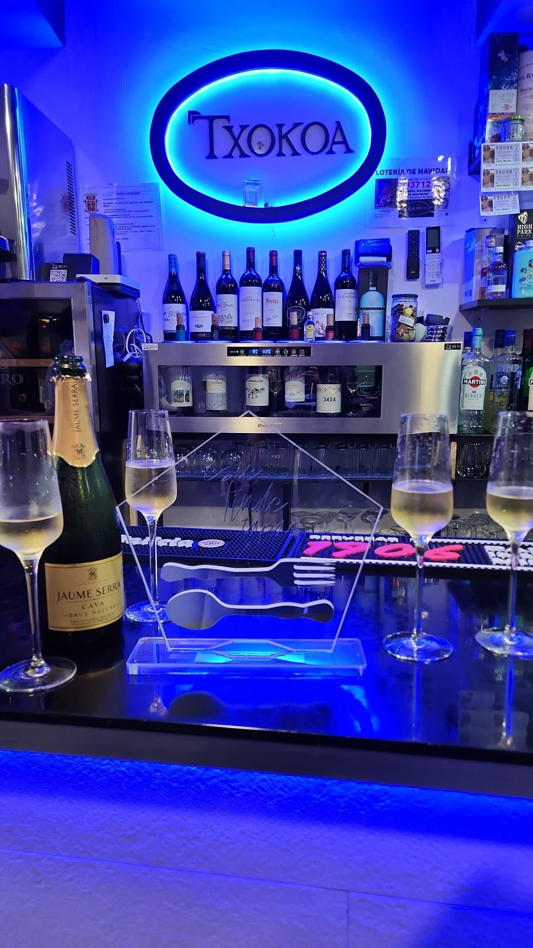 Barra con copas y botellas de cava, iluminación azul neón y logotipo 