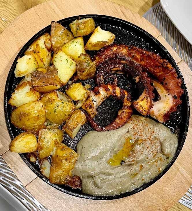 Un plato de comida con patatas y pulpo sobre una mesa de madera.
