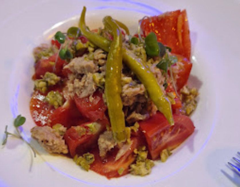 Un plato blanco cubierto con tomates, pimientos verdes y atún.