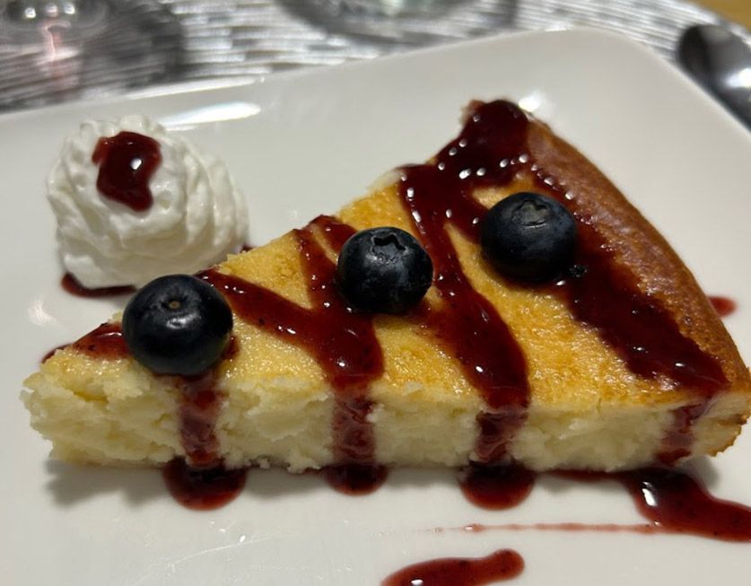 Una rebanada de tarta de queso con arándanos y crema batida en un plato blanco