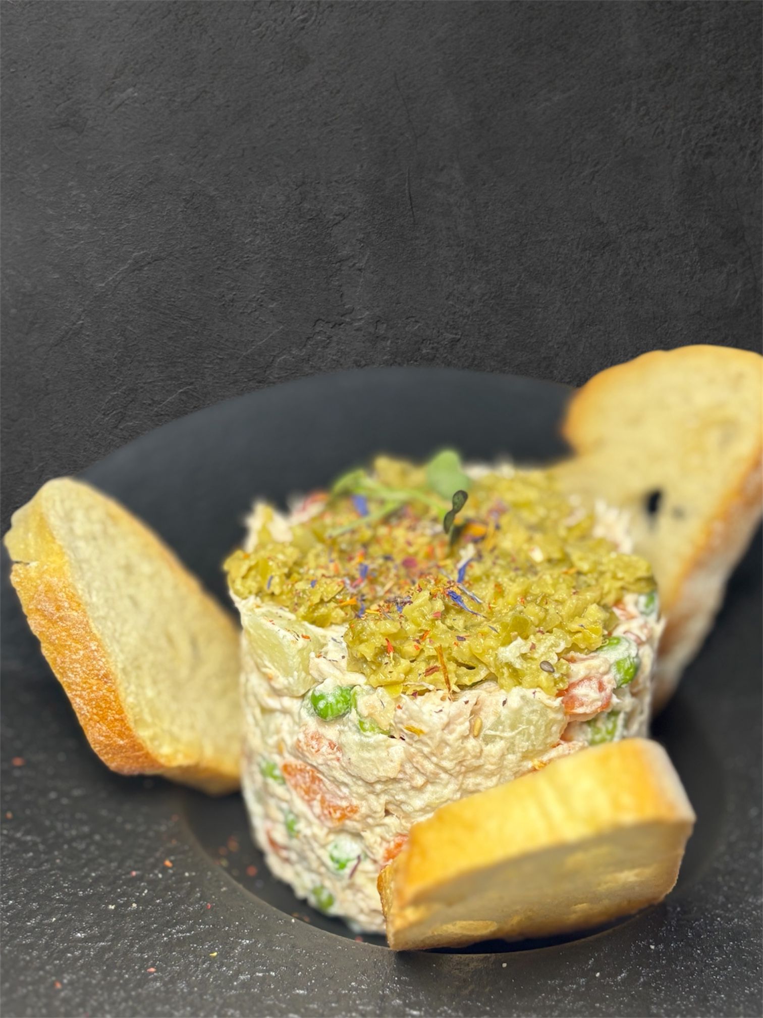 Torre de ensalada con cobertura verde y tostadas en plato negro.