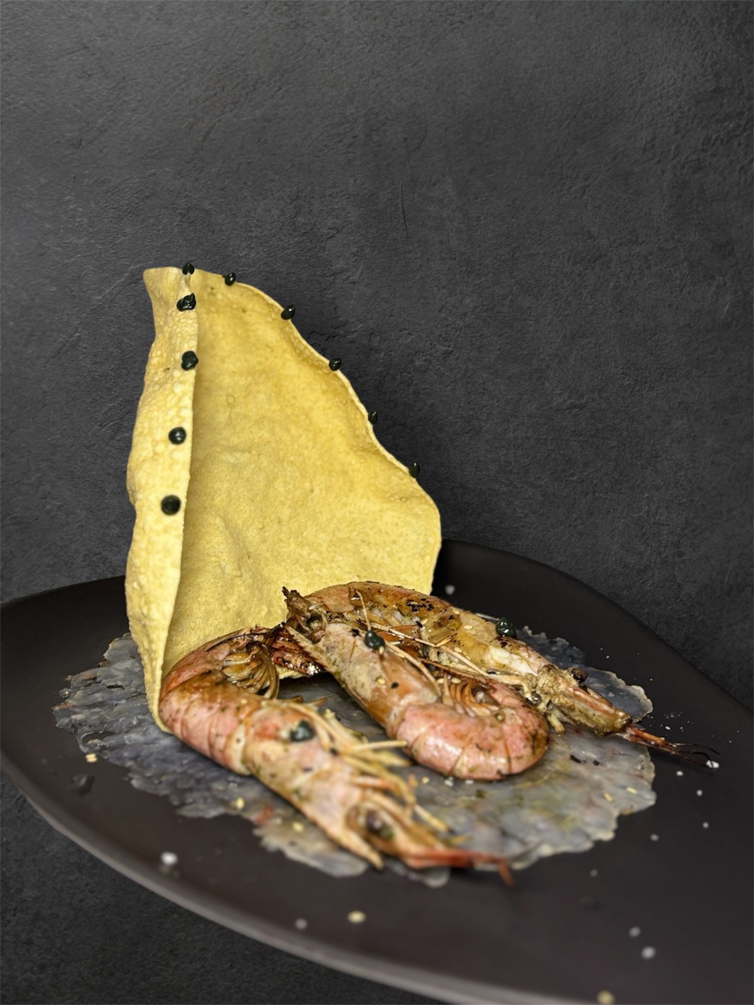 Camarones a la parrilla en un plato oscuro con una envoltura amarilla y pequeñas escamas de sal.