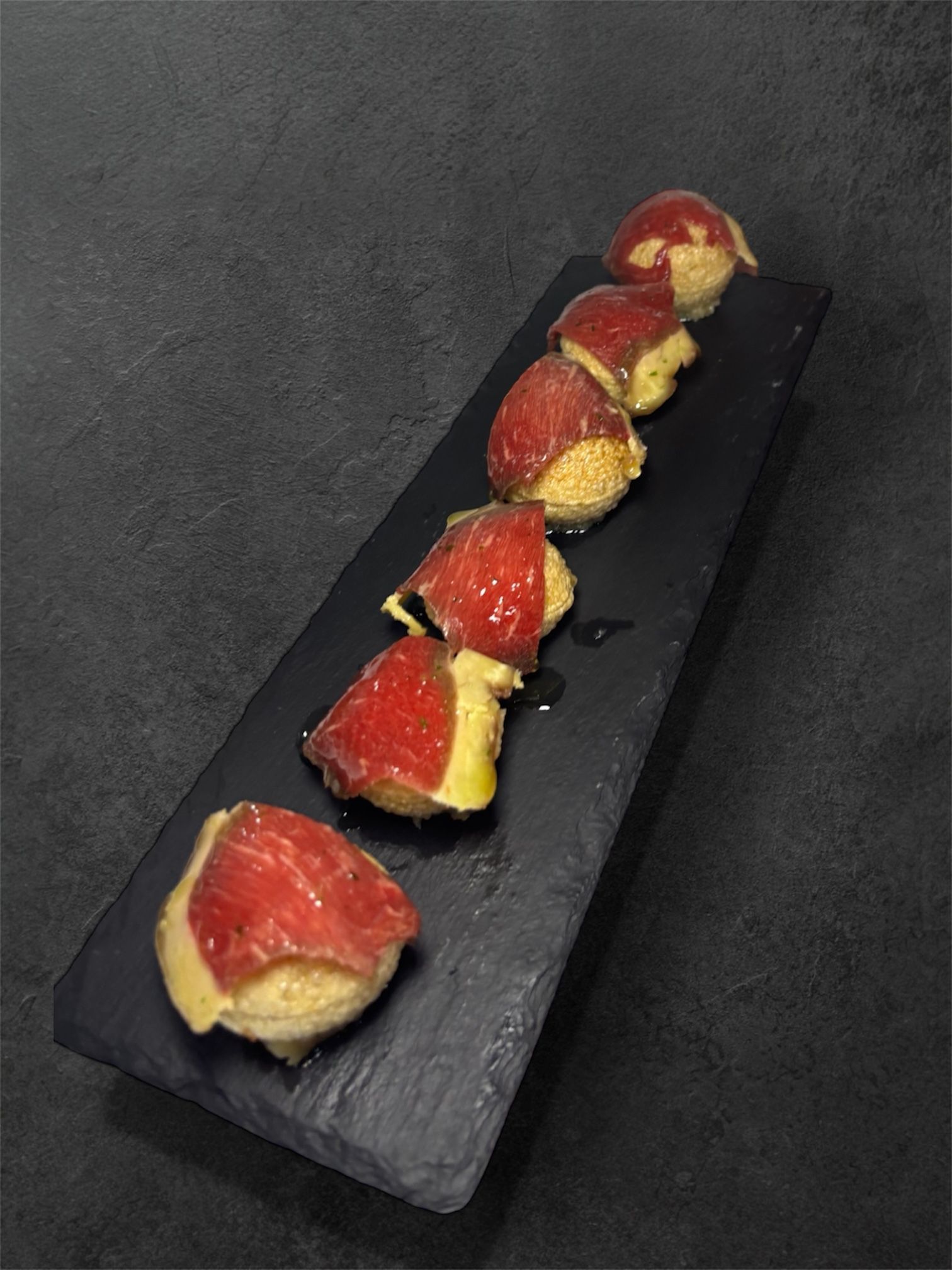 Aperitivo: bocados de queso cubiertos con carne roja, servidos sobre una pizarra negra.