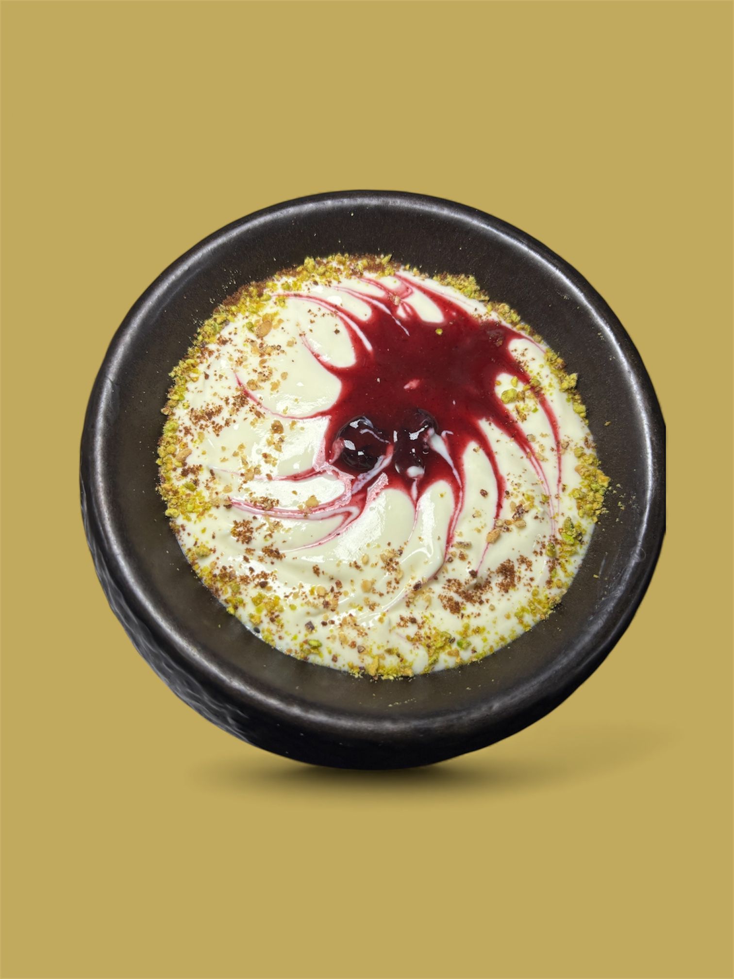 Postre cremoso en un recipiente oscuro, aderezado con salsa roja y espolvoreado con pistachos verdes.