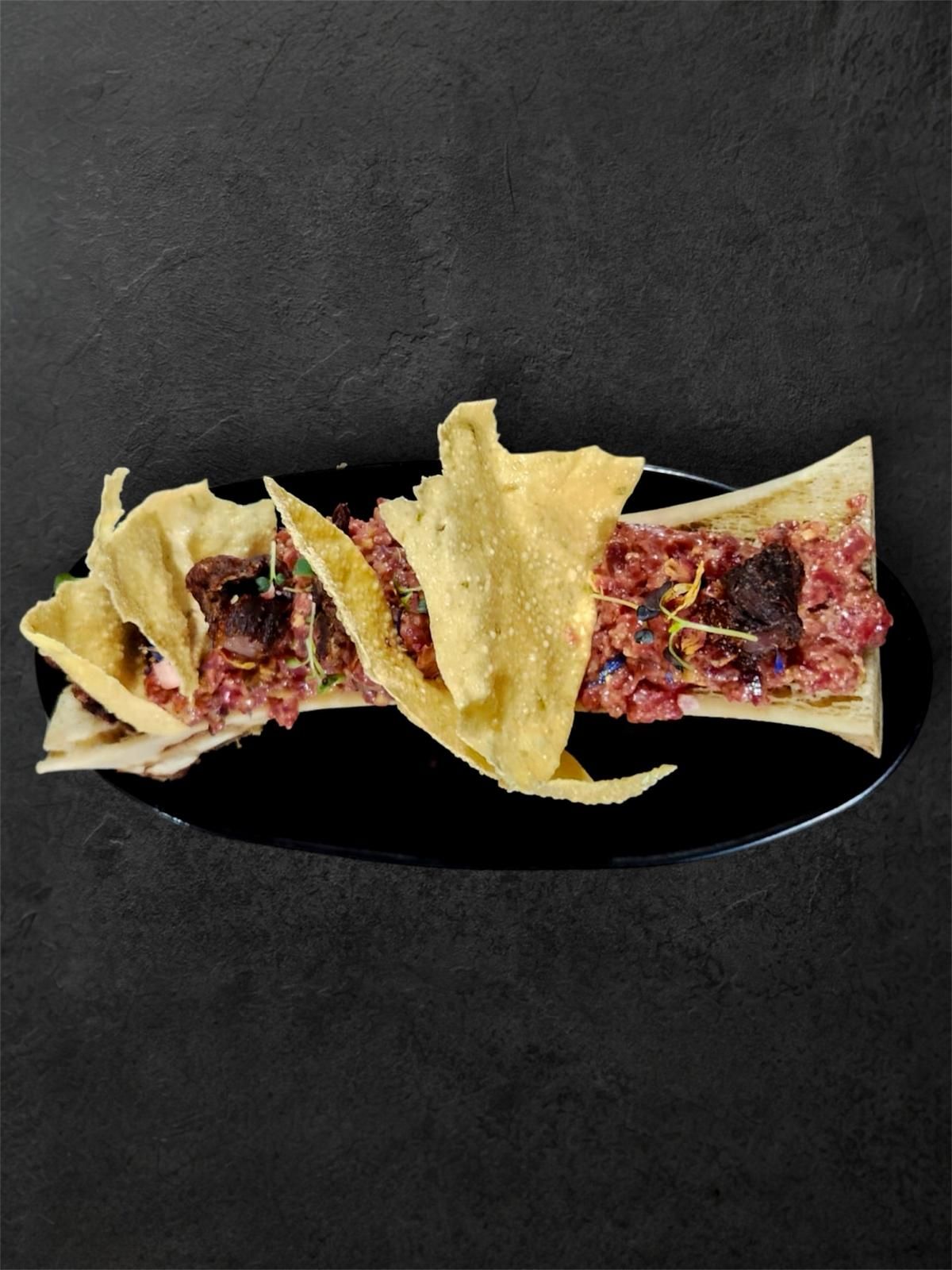 Plato de médula ósea con patatas fritas en un plato negro, sobre un fondo oscuro.
