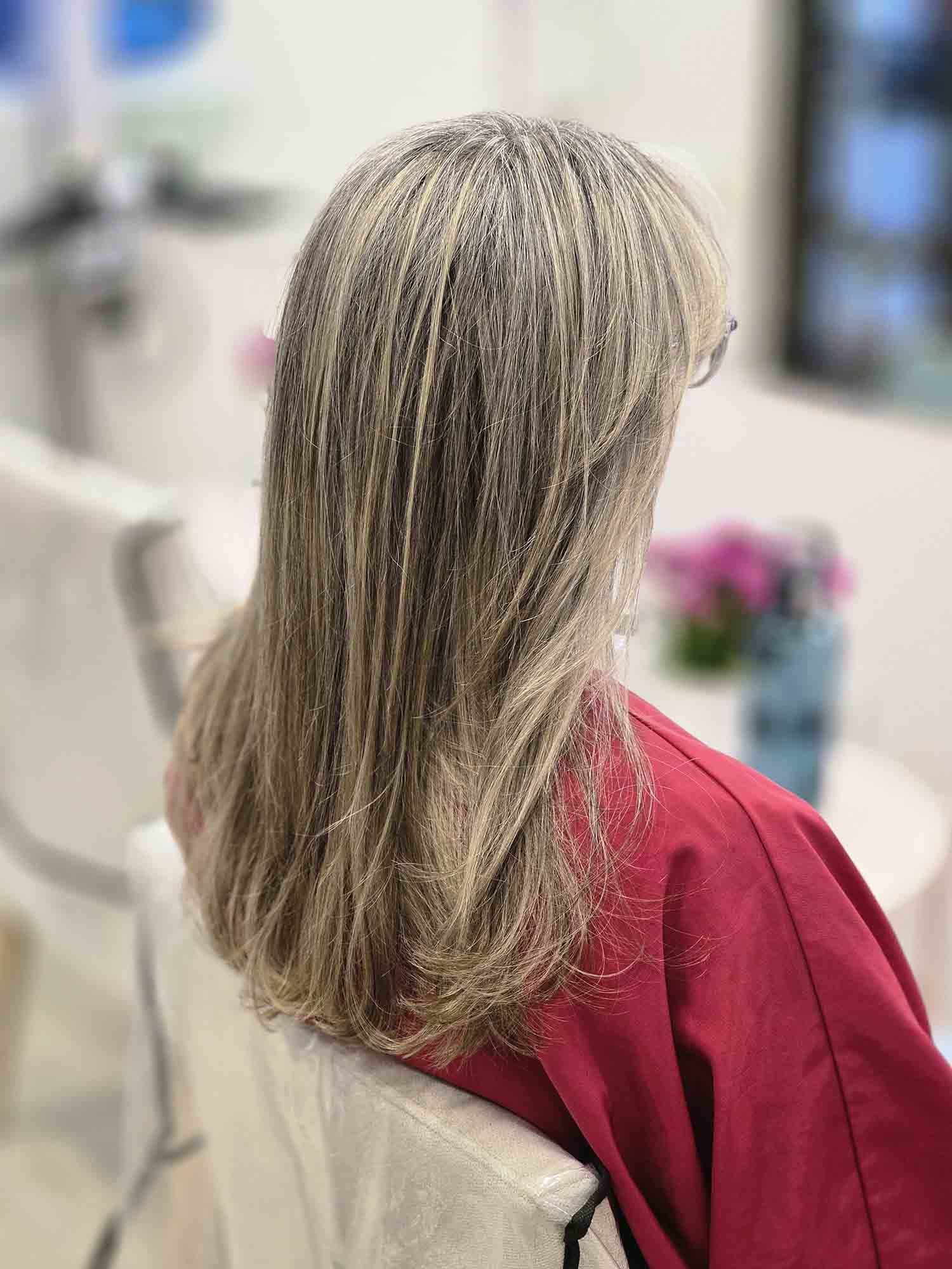 Una mujer con cabello largo y rubio está sentada en una silla en un salón.