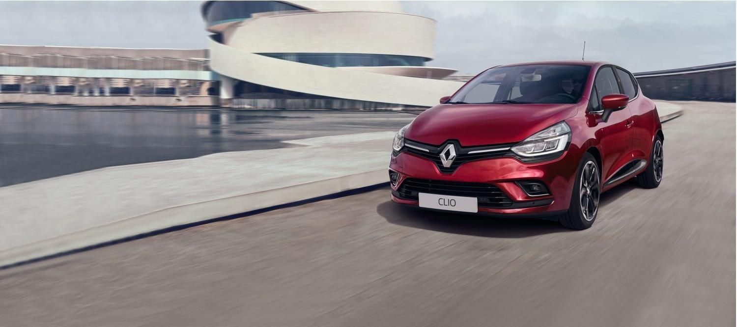 Une Renault Clio rouge circule près d'un port dans une zone urbaine.