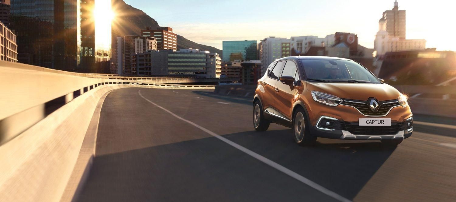 Un SUV orange circule sur un pont dans une grande ville, avec des bâtiments en arrière-plan.