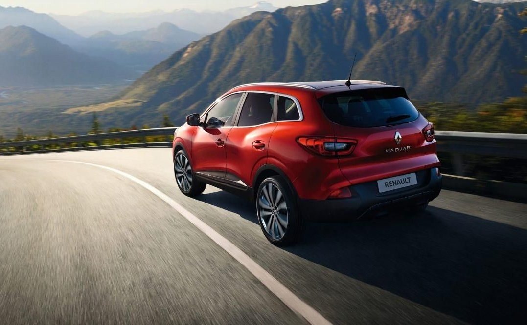 Un SUV rouge roule sur une route de montagne sinueuse avec des collines pittoresques en arrière-plan.