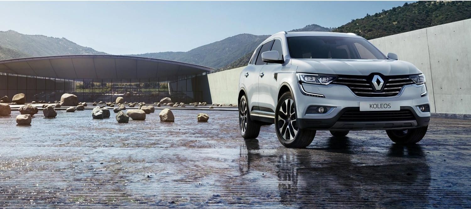 Un SUV blanc roule sur une route mouillée, avec des montagnes en arrière-plan.