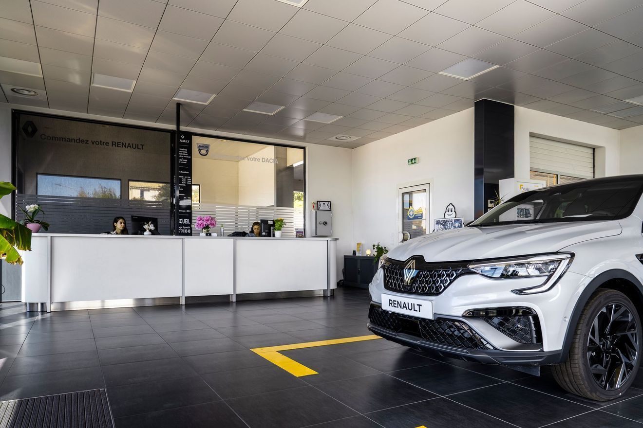 Salle d'exposition automobile avec une Renault blanche garée à l'intérieur, devant un comptoir d'accueil.