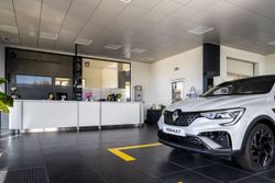 Intérieur d'un showroom automobile avec une voiture blanche garée près d'un comptoir de service.