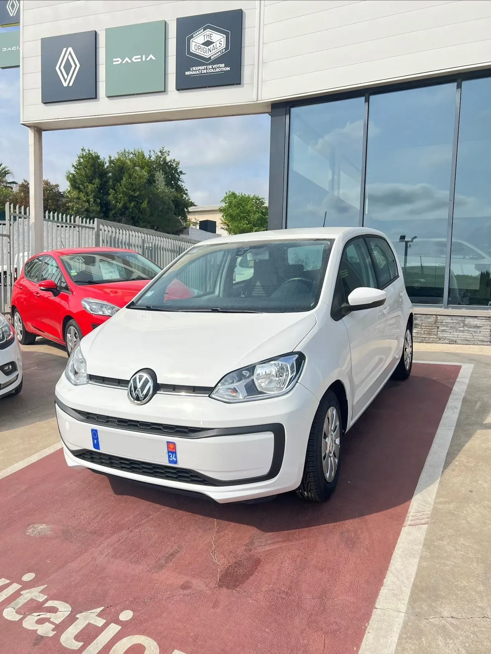 Une Volkswagen blanche est garée devant la concession face aux baies vitrées.