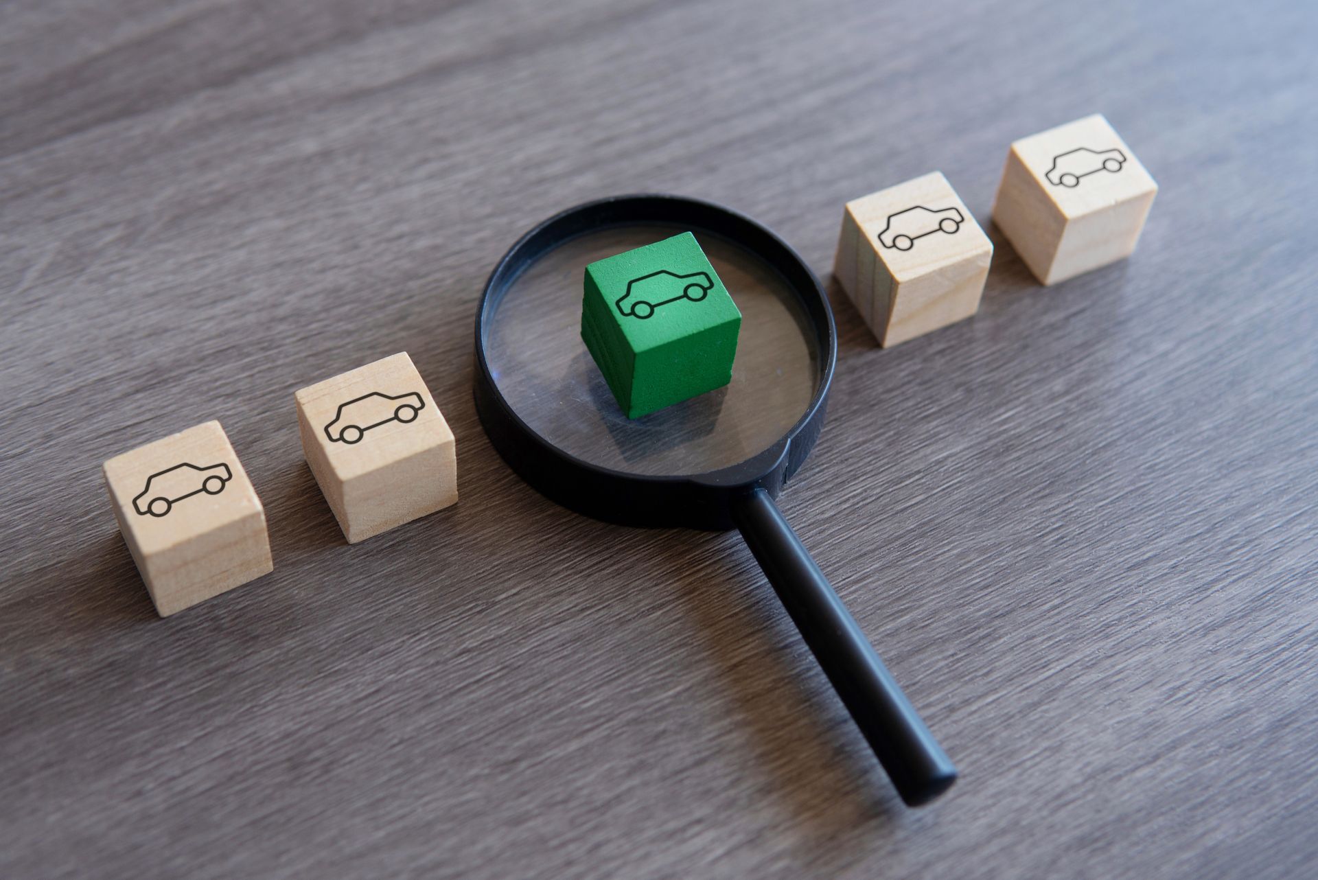 5 blocs de bois avec des voitures gravées sont posés sur bureau. L'un d'eux est vert et mis en évidence par une loupe.