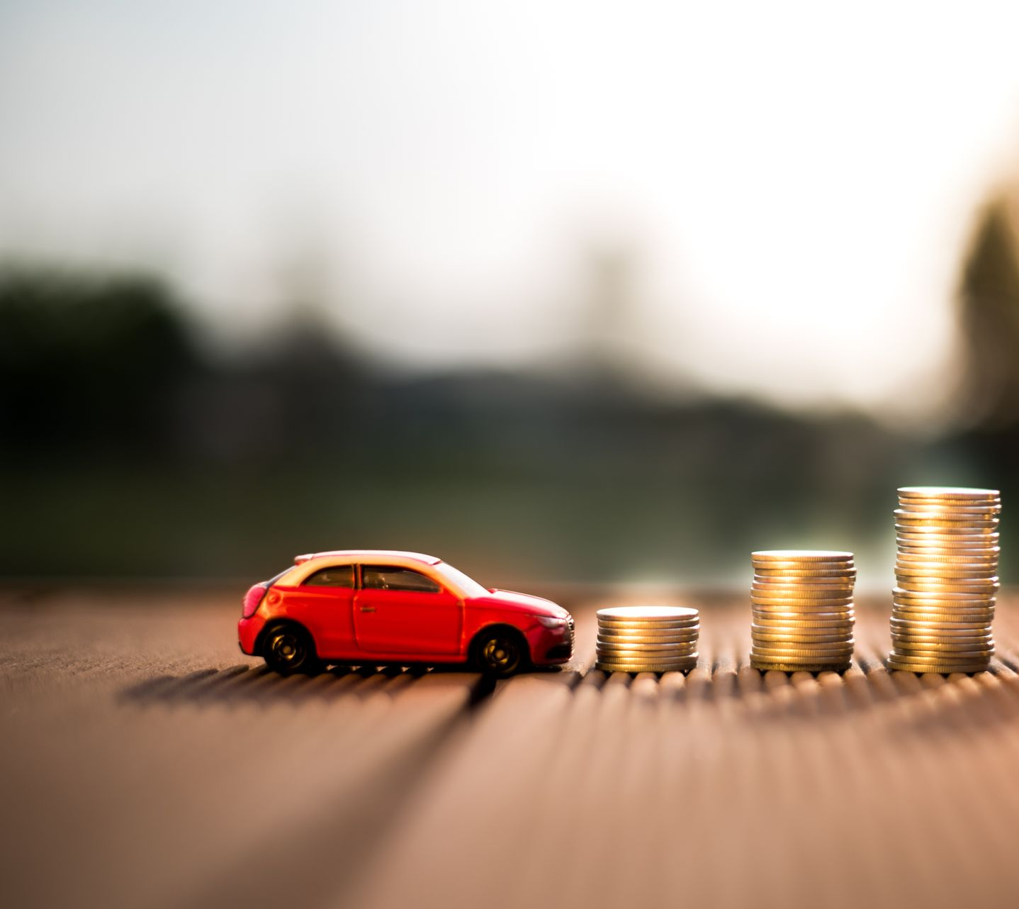 Une petite voiture rouge à côté de piles de pièces d'or sur une table.